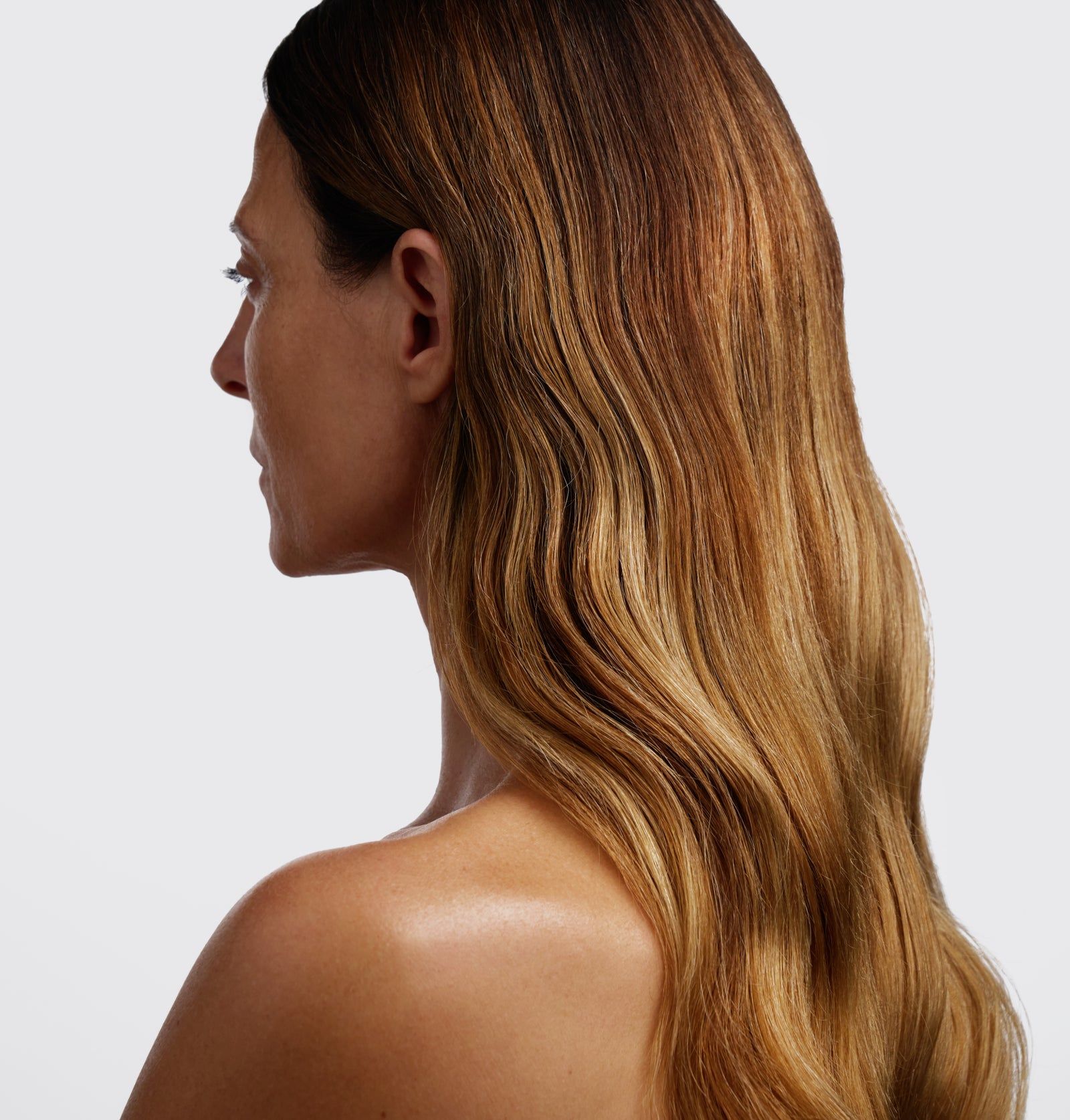 Profil einer Frau mit schulterlangem, gewelltem Haar. Die Haare sind braun mit helleren Strähnen. Der Hintergrund ist weiß.