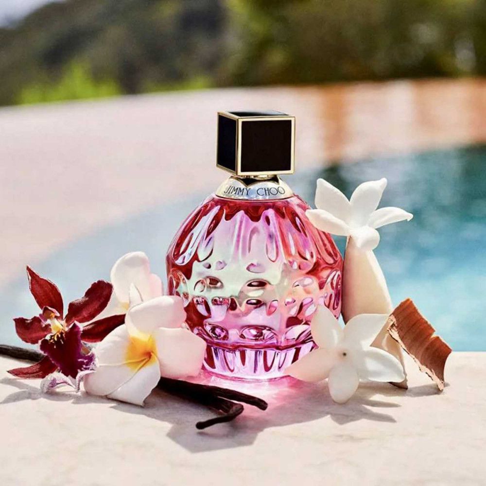 Rosa Flakon mit schwarzem Deckel, umgeben von Blüten und Vanilleschoten. Hintergrund: Wasser.