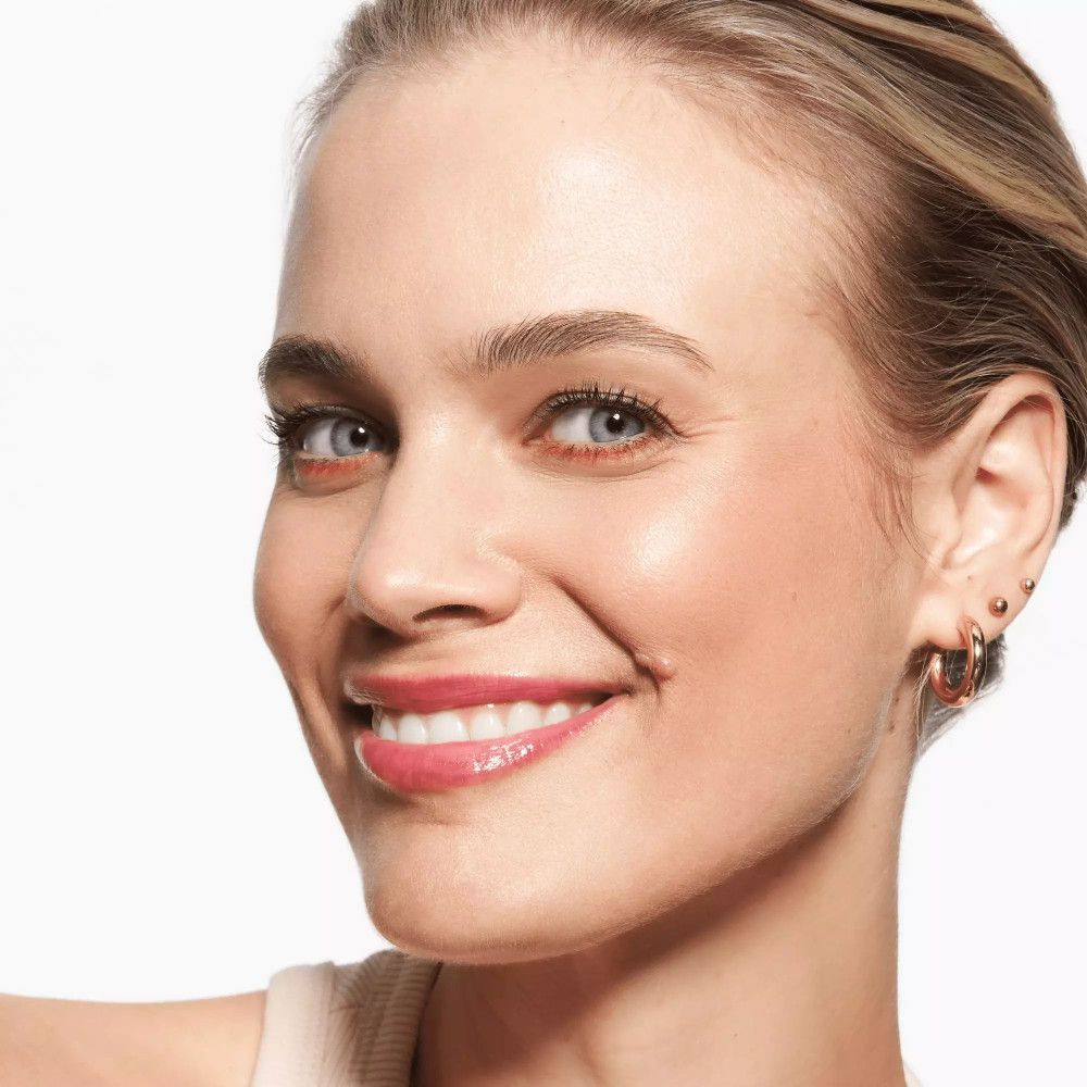 Nahaufnahme einer lächelnden Frau mit rosafarbenen Lippen. Sie trägt Make-up und Ohrringe.