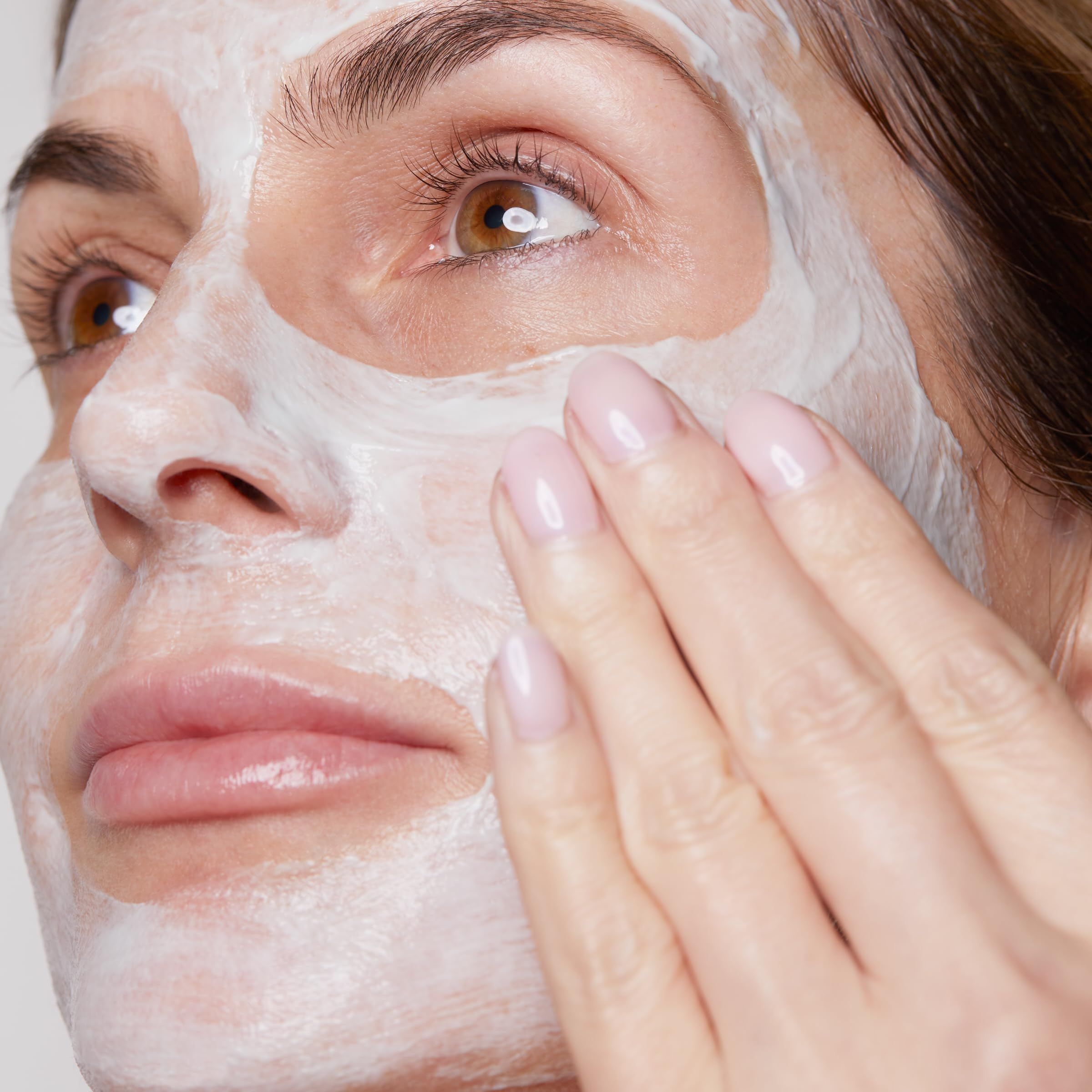Frau trägt Gesichtsmaske. Hand berührt Gesicht. Maske ist weiß. Haut ist sichtbar.