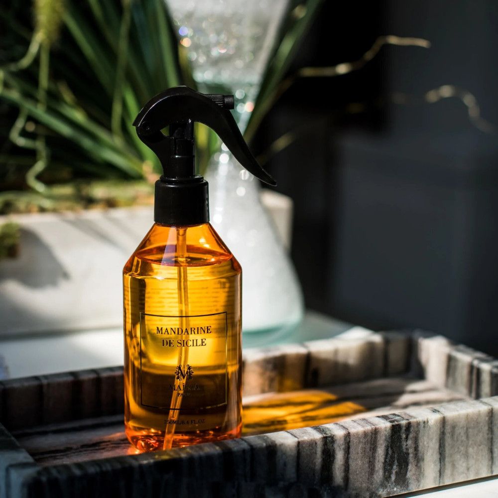 Bernsteinfarbene Sprühflasche mit schwarzem Sprühkopf. Aufschrift: Mandarine de Sicile. Steht auf einem Tablett.