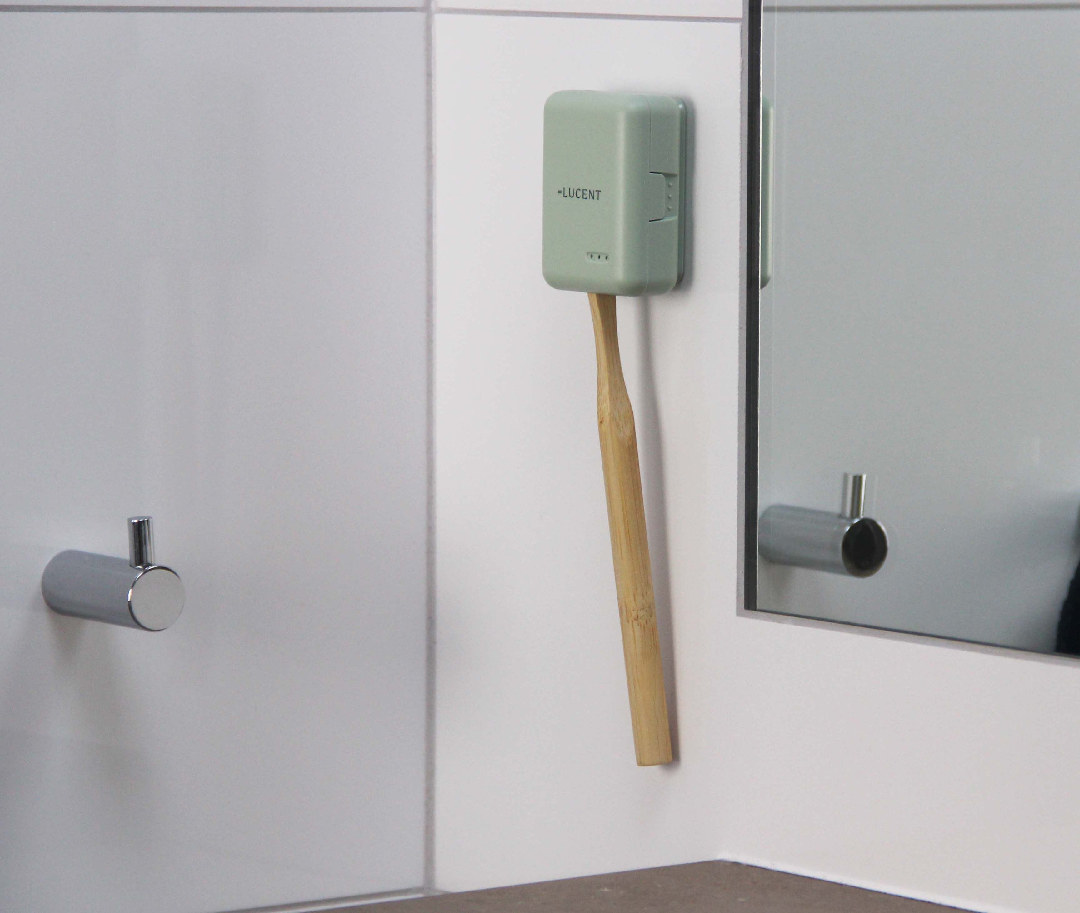 Hellgrünes Etui an der Wand. Zahnbürste steckt im Etui. Spiegel im Hintergrund.