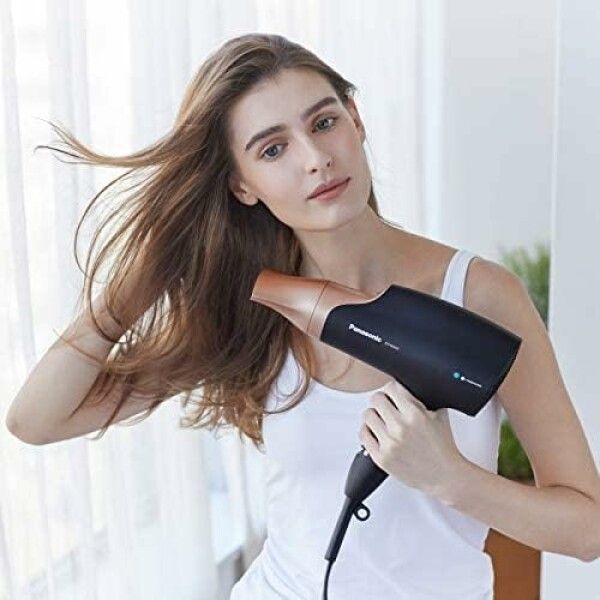 Frau hält einen schwarzen Haartrockner mit roségoldfarbener Düse. Marke Panasonic, Modell EH-NA63. Sie trocknet ihre Haare.