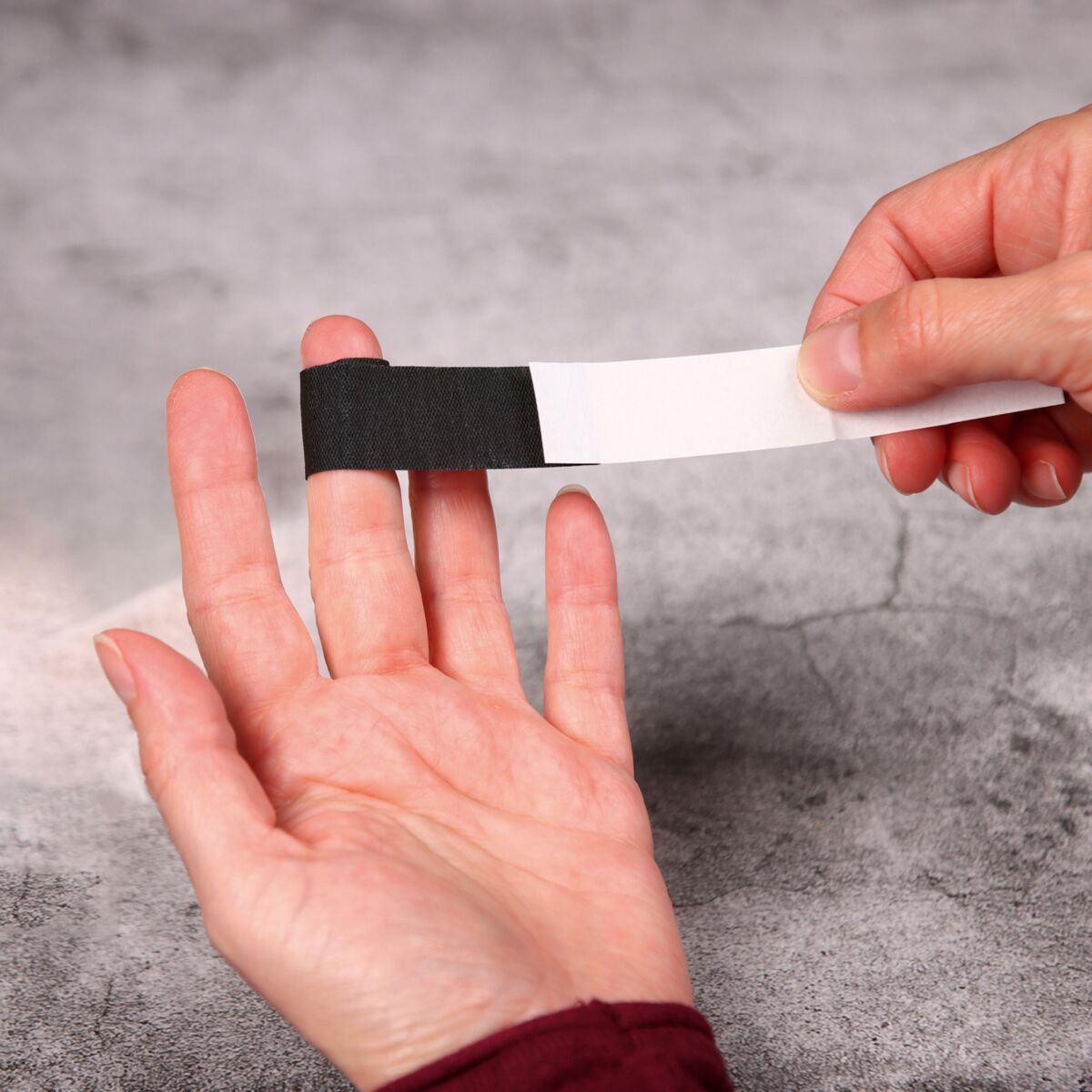 Hand wendet ein schwarzes, elastisches WERO PowerTex Fingerpflaster auf einen Finger.