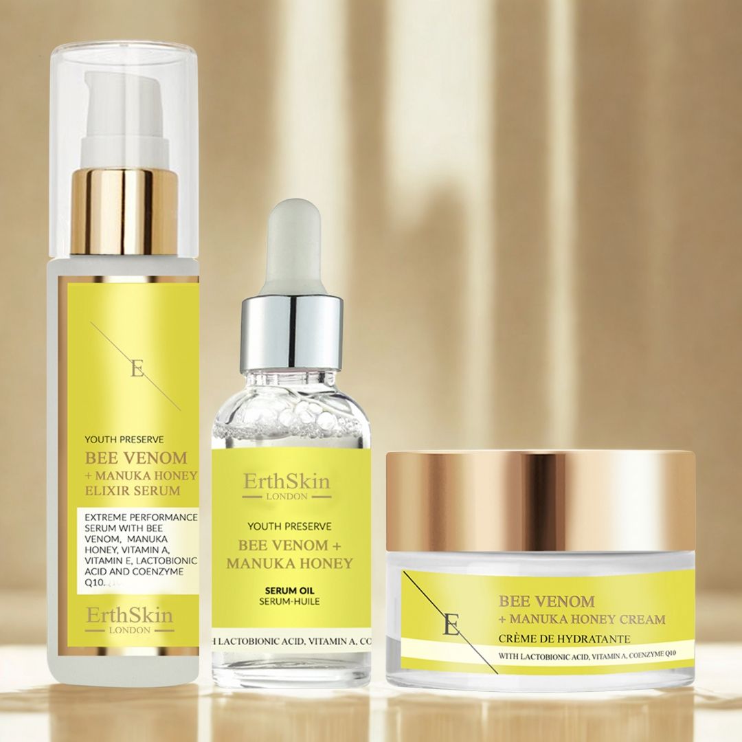 Drei Kosmetikprodukte von ErthSkin London. Flaschen und Tiegel mit gelben Etiketten und goldenen Deckeln. Beschriftung: Bienengift + Manuka-Honig.