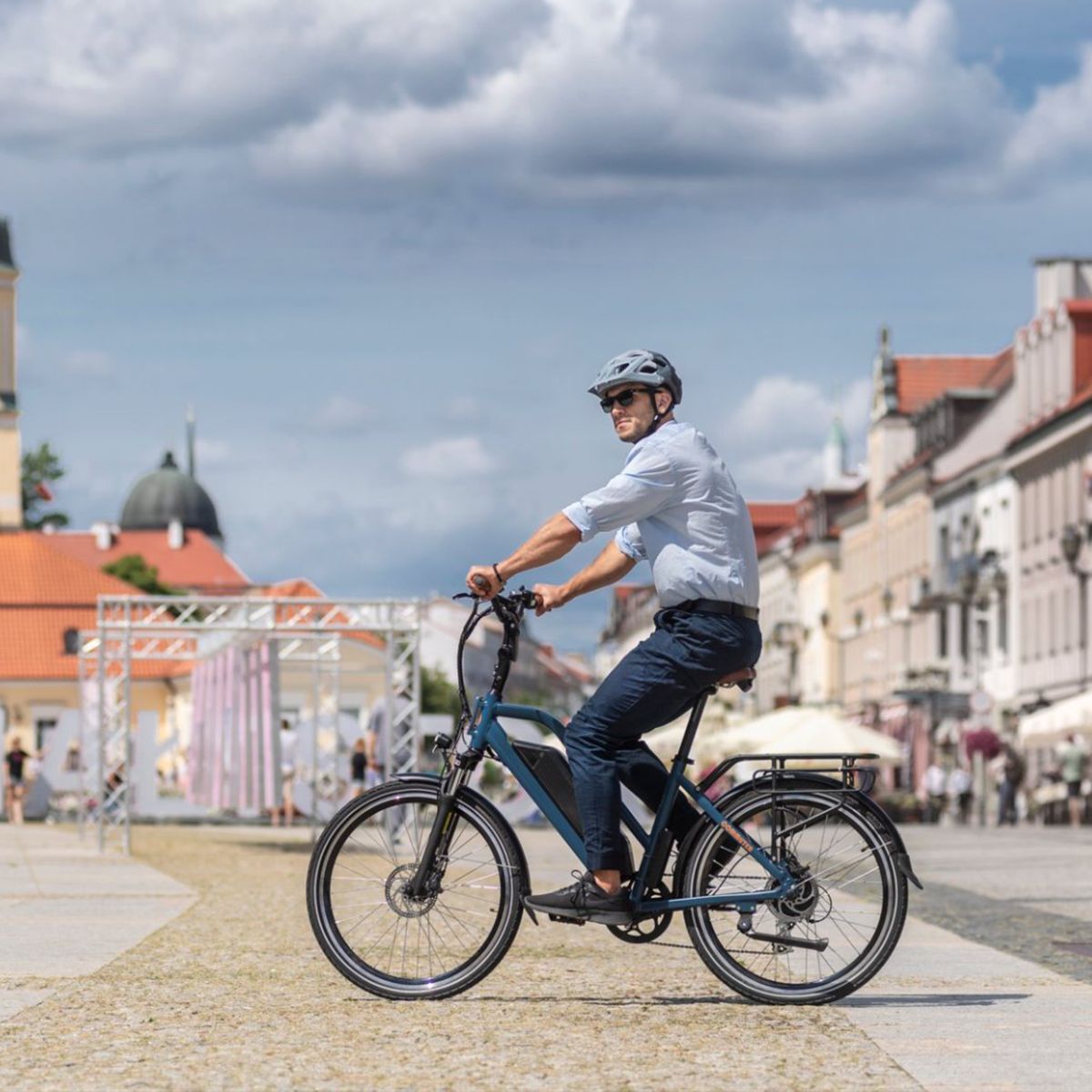 Mann fährt auf einem blauen E-Bike durch eine Stadt. Helm, Sonnenbrille.