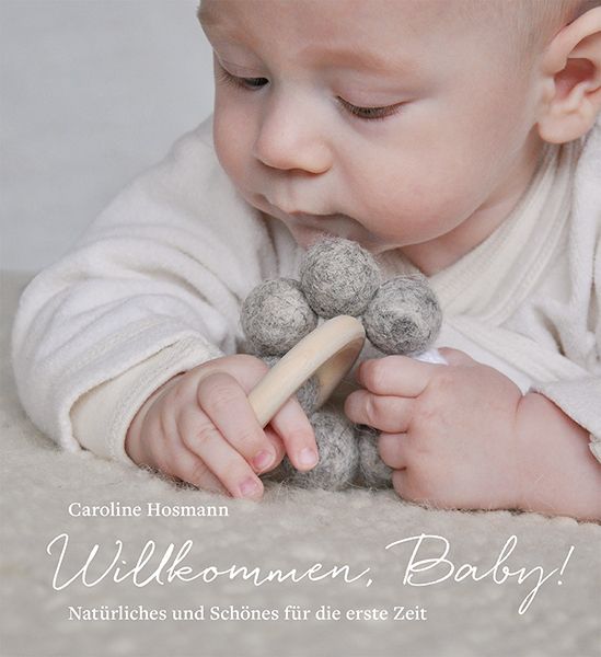 Baby hält Spielzeug. Graue Kugeln an Holzgriff. Text: Willkommen, Baby! Natürliches und Schönes für die erste Zeit. Autorin: Caroline Hosmann.