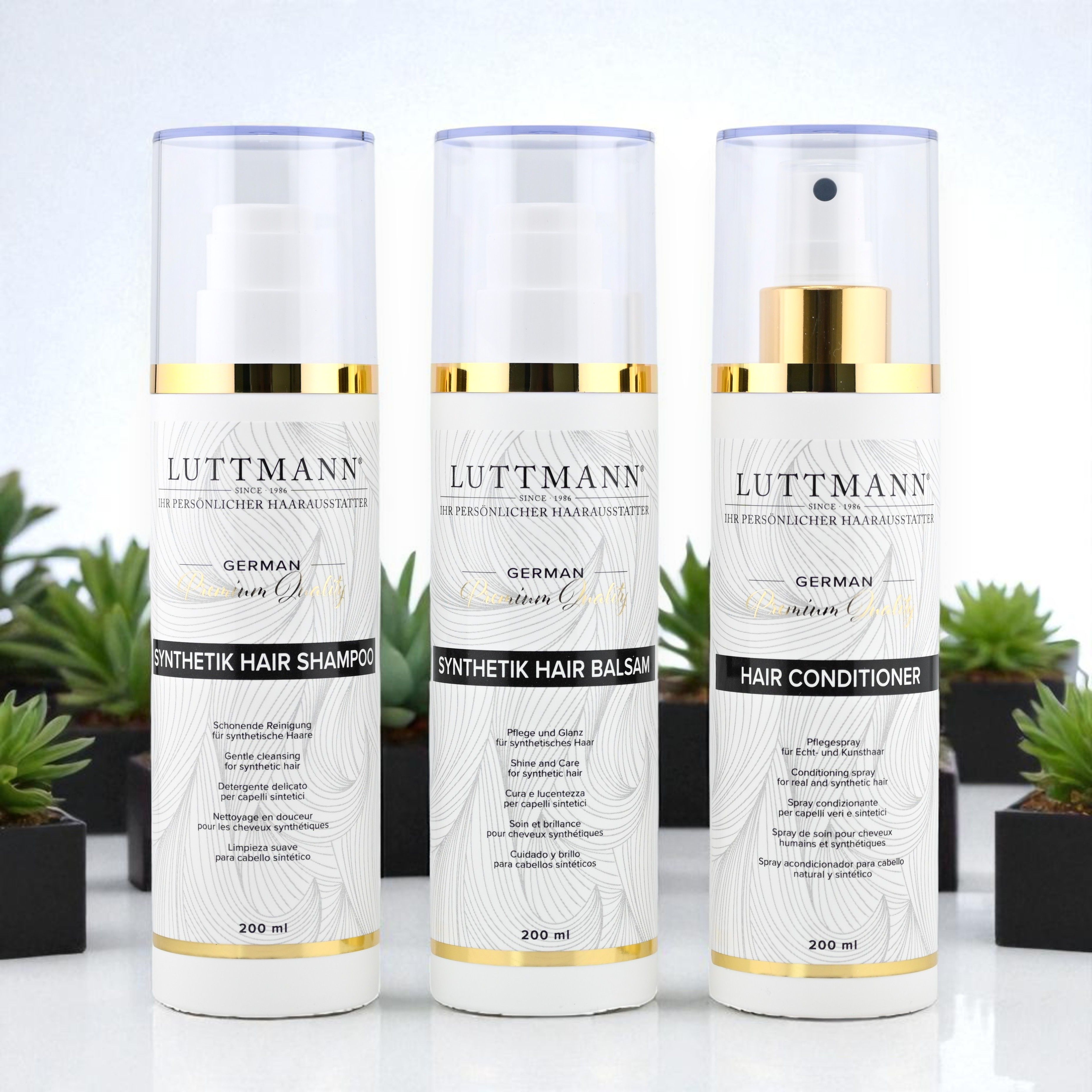 Drei Flaschen LUTTMANN® Synthetik Hair Pflegeset: Shampoo, Balsam und Hair Conditioner. Weiße Flaschen mit goldenen Akzenten, vor Pflanzen.