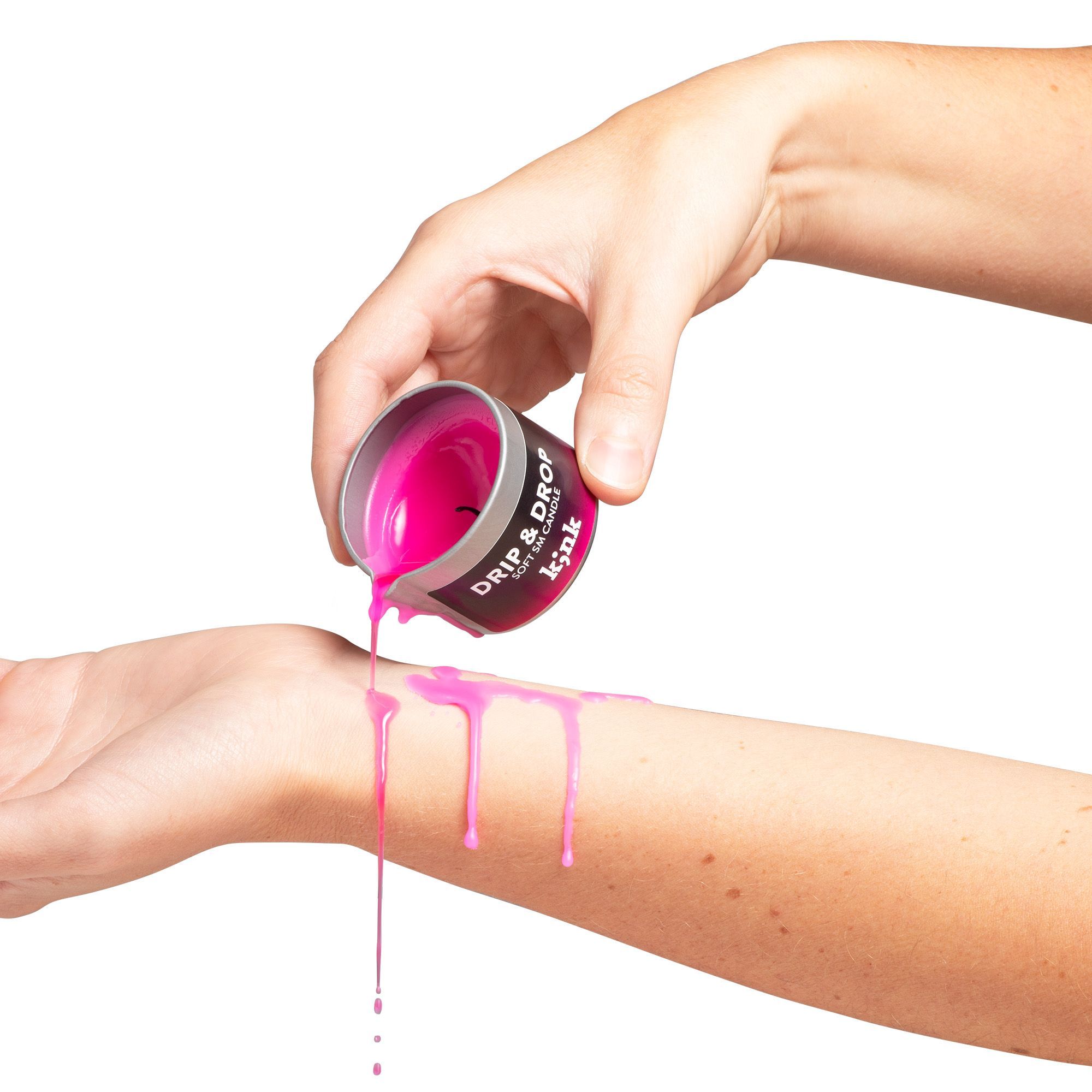 Eine Hand gießt geschmolzenes, pinkfarbenes Wachs aus einem Behälter auf ein Handgelenk. Auf dem Behälter steht "Drip & Drop".