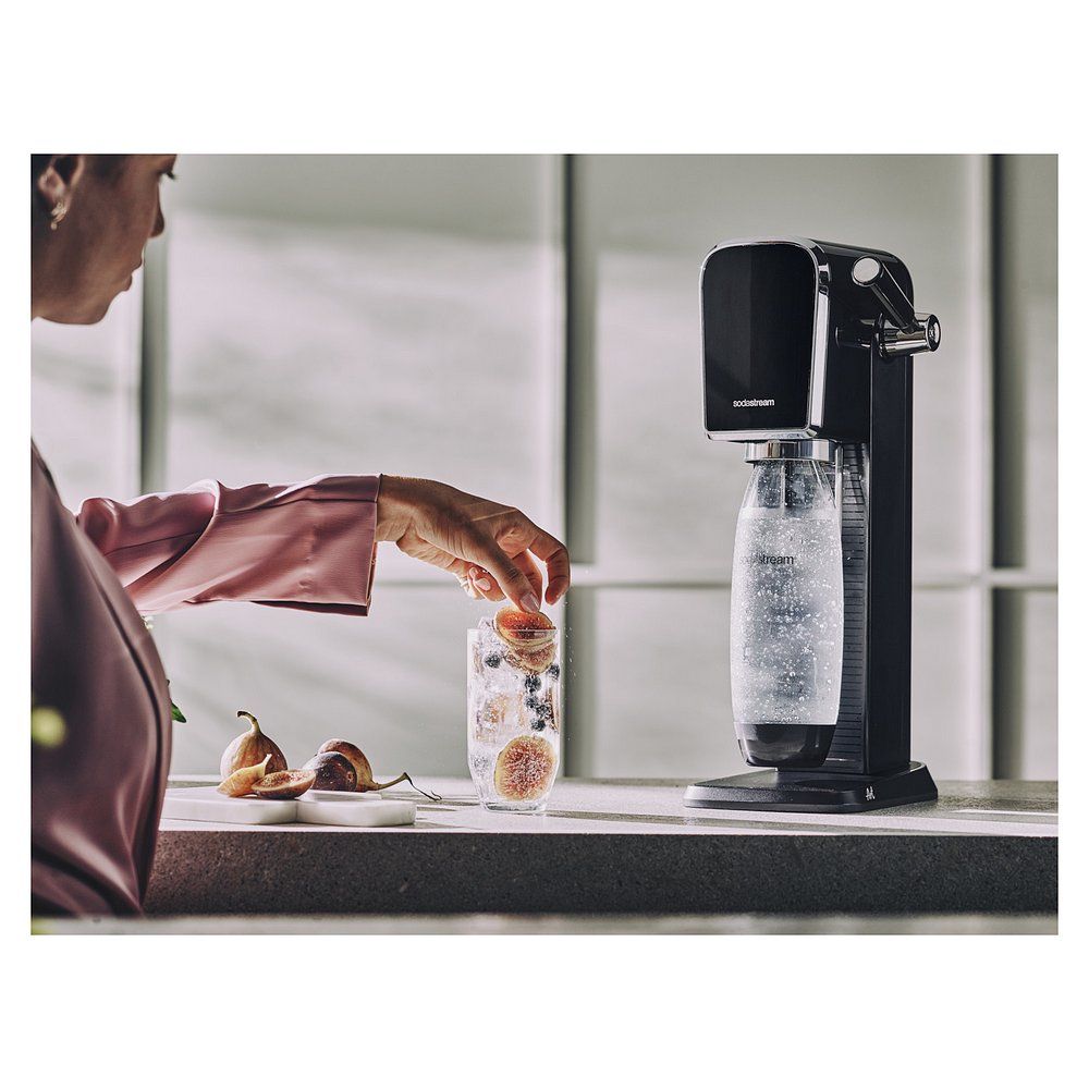 Frau gibt Früchte in ein Glas mit Eis und Wasser neben SodaStream Art.
