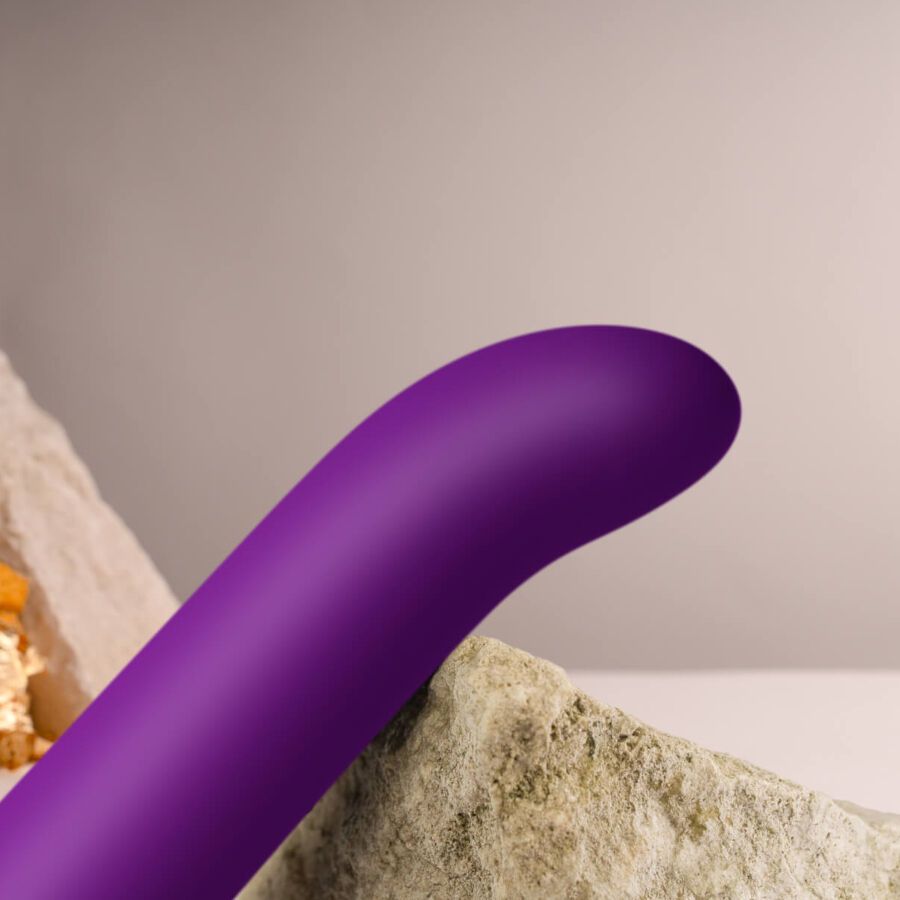 Lila Vibrator mit gebogener Form. Auf einem Stein platziert.