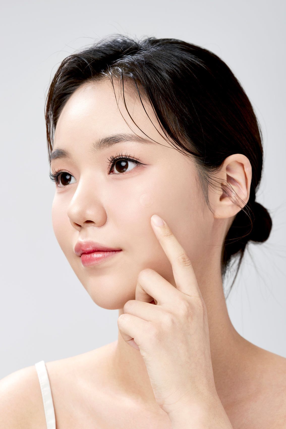 Porträt einer Frau, die mit dem Finger auf ihre Wange zeigt. Helle Haut, dunkle Haare.