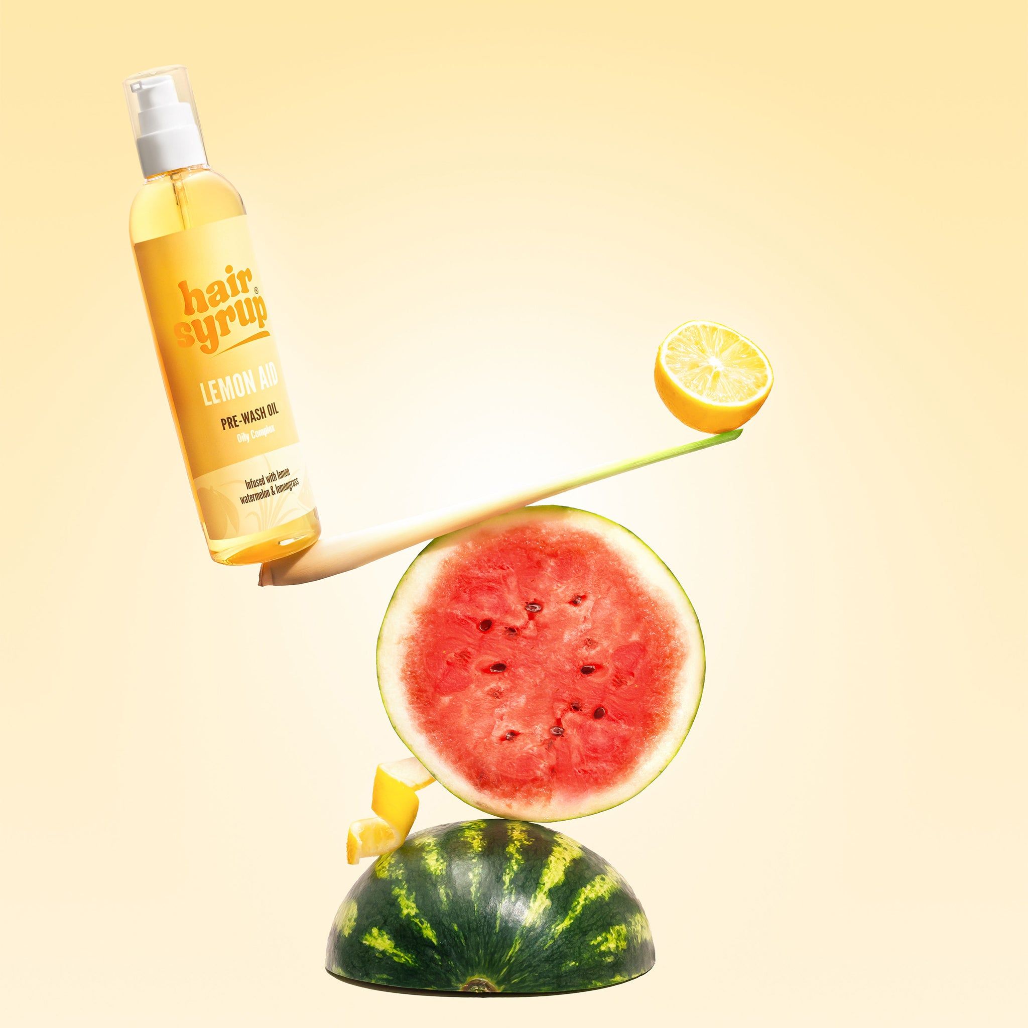 Gelbe Flasche mit Produktetikett, ausbalanciert mit Wassermelone und Zitrone. Text: Hair Syrup Lemon-Aid.