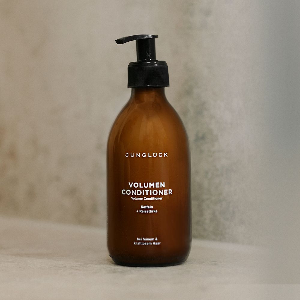 Braune Flasche mit schwarzem Pumpkopf. Aufschrift: JUNGLÜCK, VOLUMEN CONDITIONER, Kaffein + Reisstärke. Für feines & kraftvolles Haar.