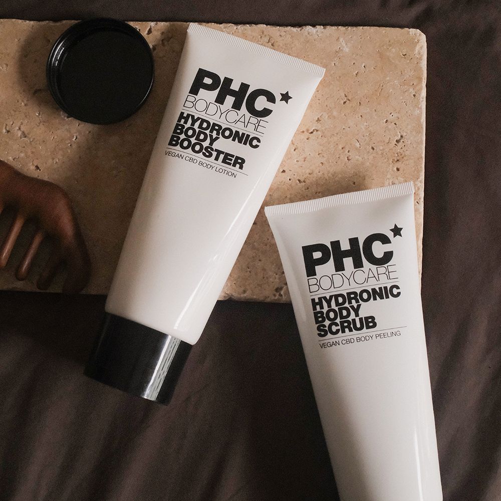 Zwei weiße Tuben: PHC Bodycare Hydronic Body Booster und Hydronic Body Scrub. Schwarze Schrift. Vegan CBD Body Lotion und Peeling.