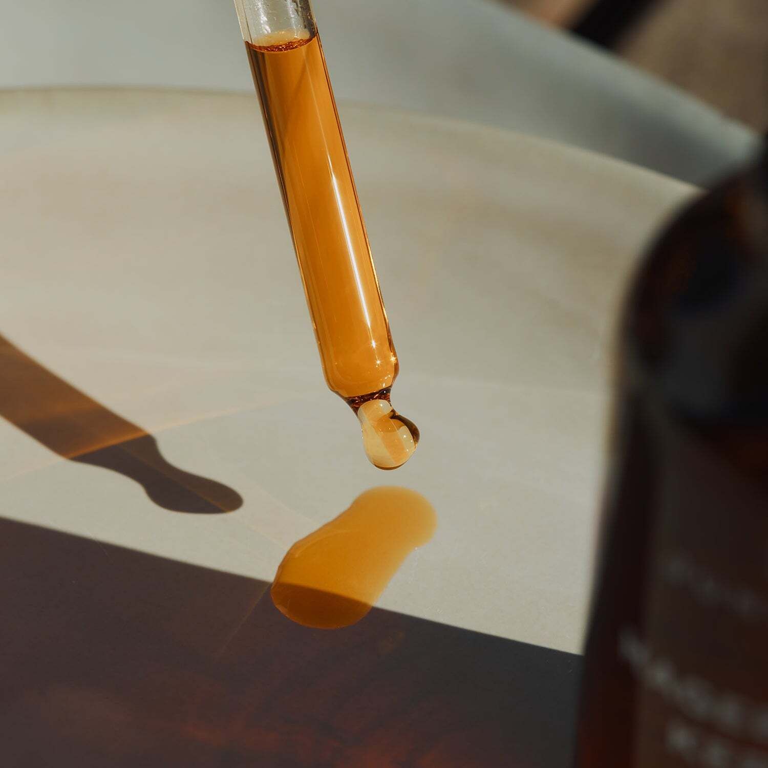 Pipette mit orangefarbenem Öl, das auf eine helle Oberfläche tropft. Im Hintergrund: Flasche mit Aufschrift JUNGLÜCK Hagebuttenkernöl.