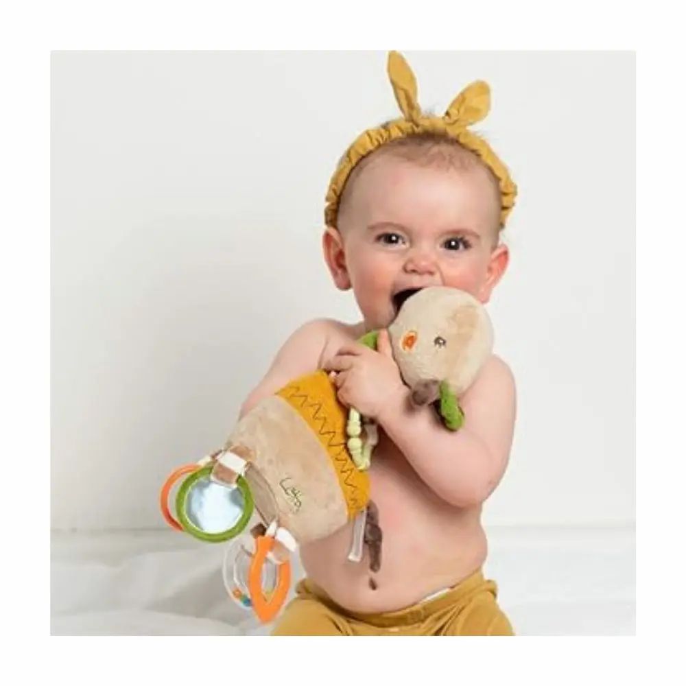 Baby beißt auf Kuscheltier-Giraffe. Beige, grün und gelb. Mit Ringen und Spiegeln. Aufschrift "Lotta". Baby trägt Stirnband.