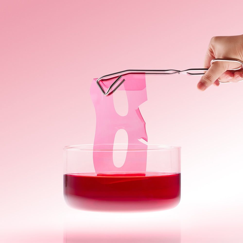 Rosa Hydrogel-Maske wird mit einer Pinzette aus roter Flüssigkeit gehoben.