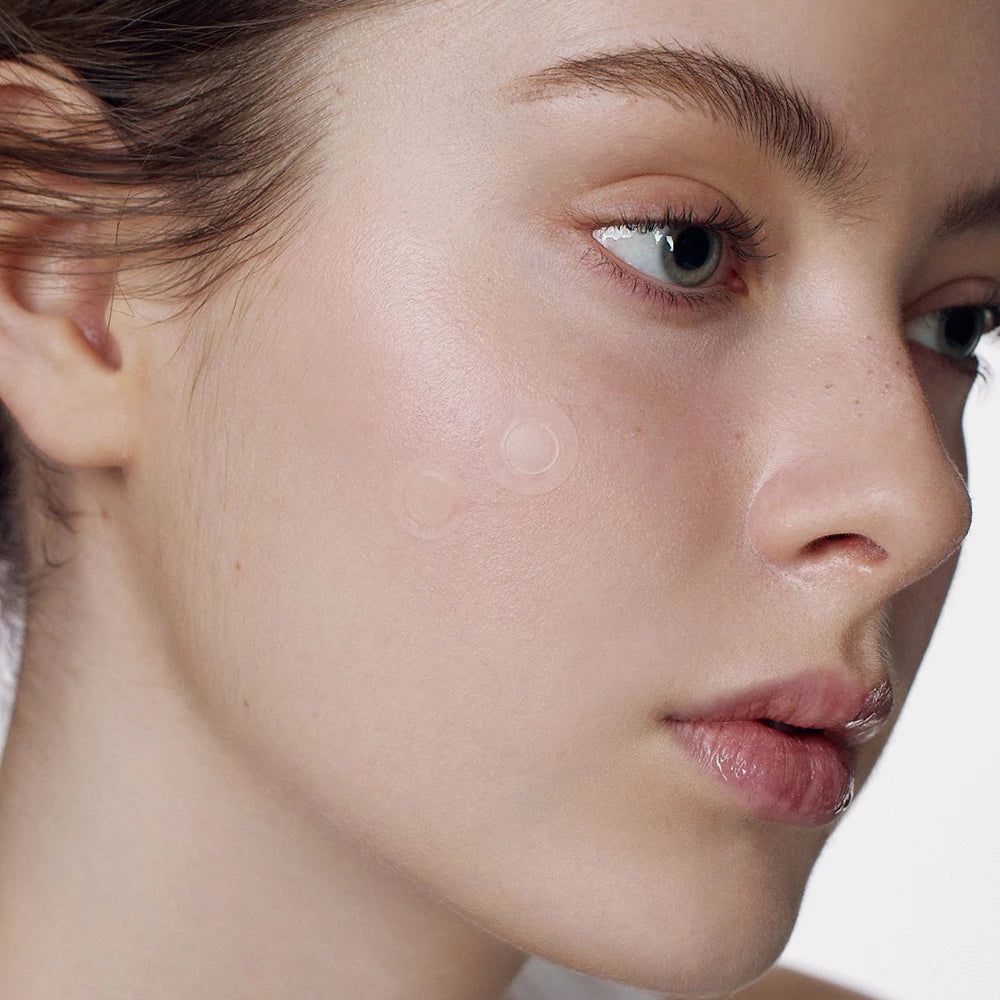 Gesicht einer Person mit einem transparenten, runden Pflaster auf der Haut. Das Pflaster hat eine strukturierte Mitte.