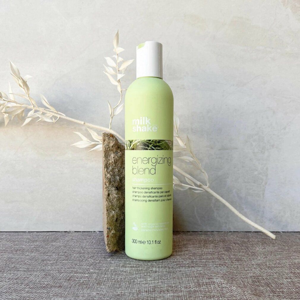 Hellgrüne Shampoo-Flasche mit weißem Deckel. Aufschrift: energizing blend shampoo. Neben einem Stein und Zweig.