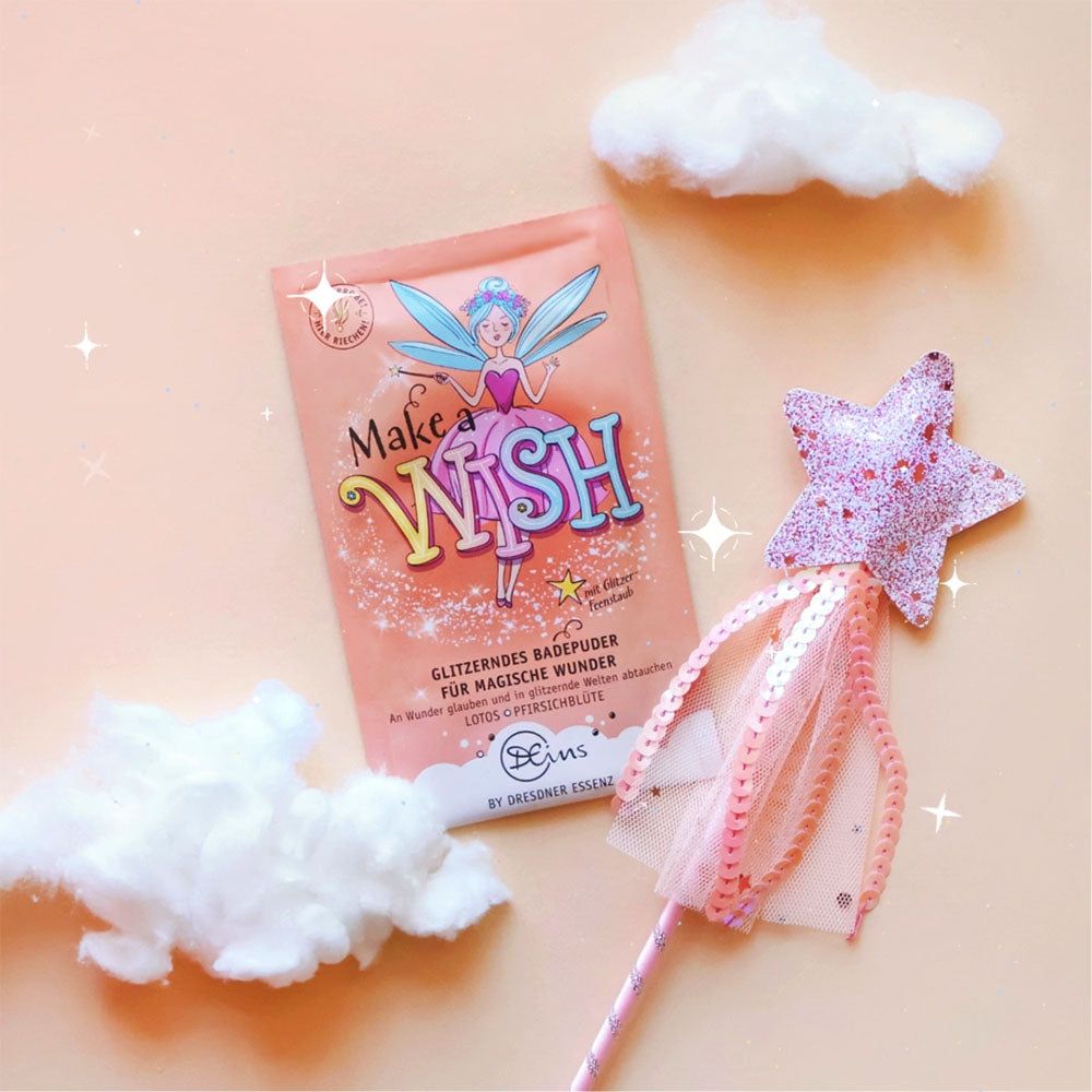Roze badzoutzakje, toverstaf en wolken op roze achtergrond. Zakje met opdruk "Make a Wish". Tekst: Glitterende badpoeder. Merk: Dresdner Essenz.