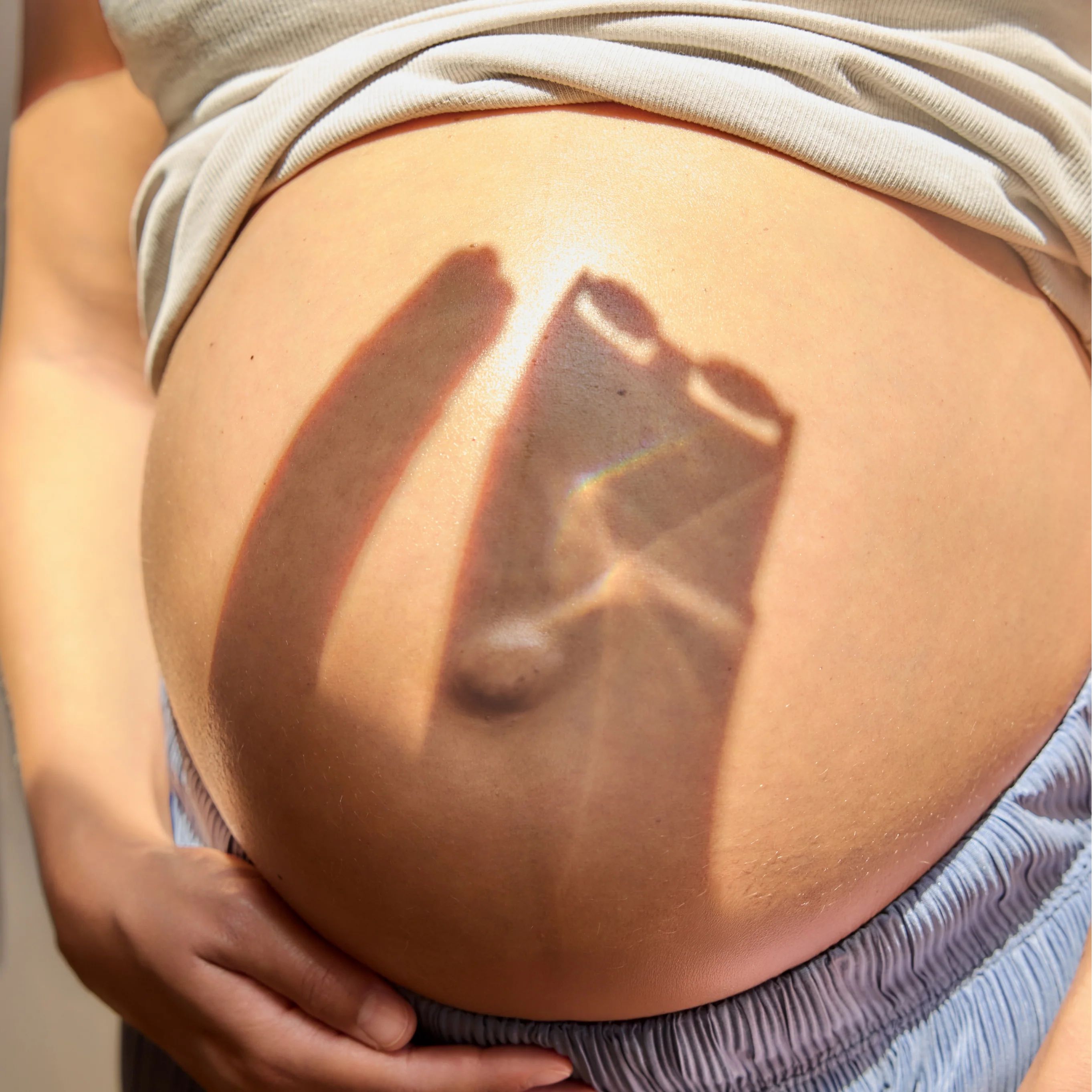Schwangere Frau, Bauch im Sonnenlicht. Schatten des Massageaufsatzes.