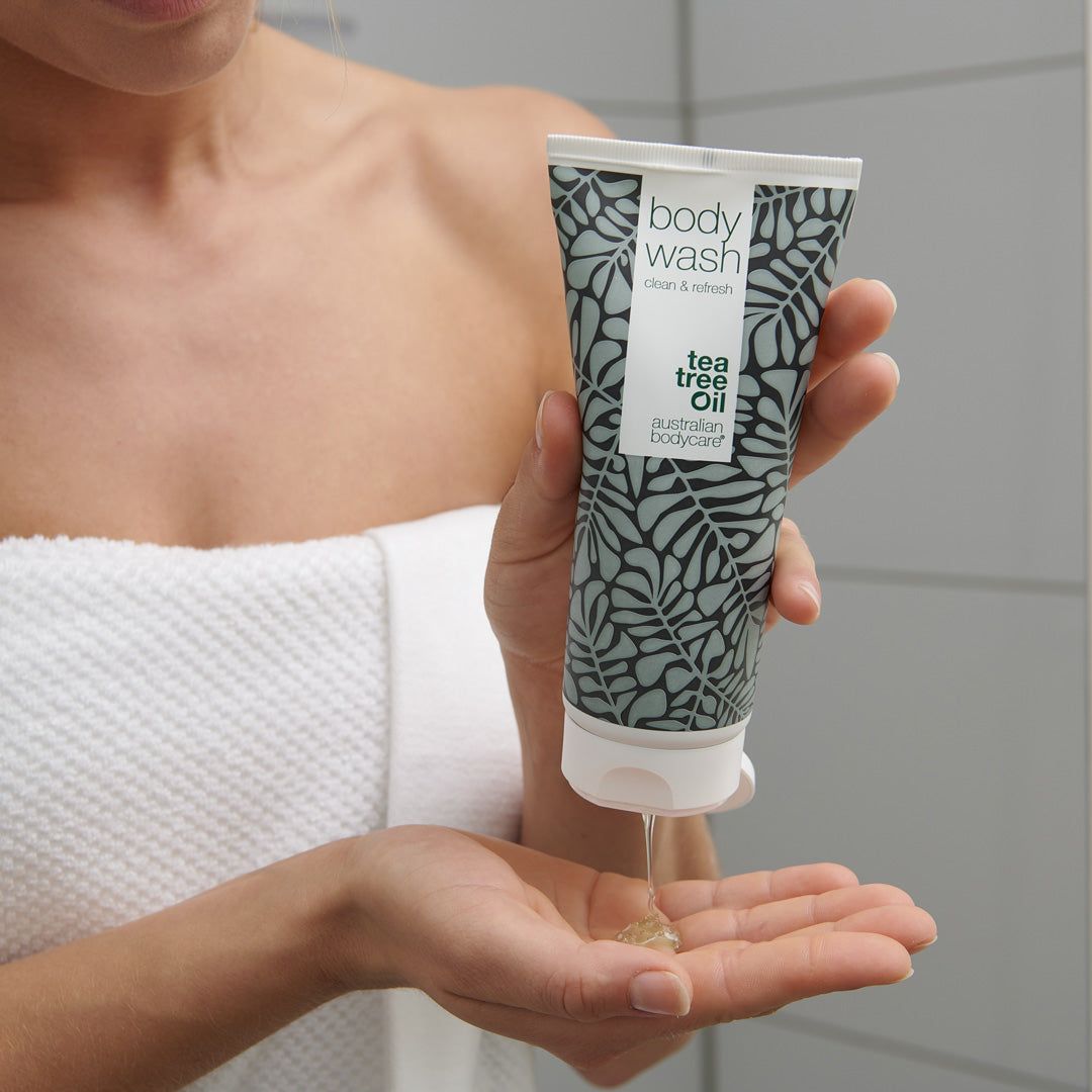 Person hält Tube Body Wash. Produkt wird auf die Handfläche gegossen. Marke: Australian Bodycare. Hintergrund: Badezimmer.