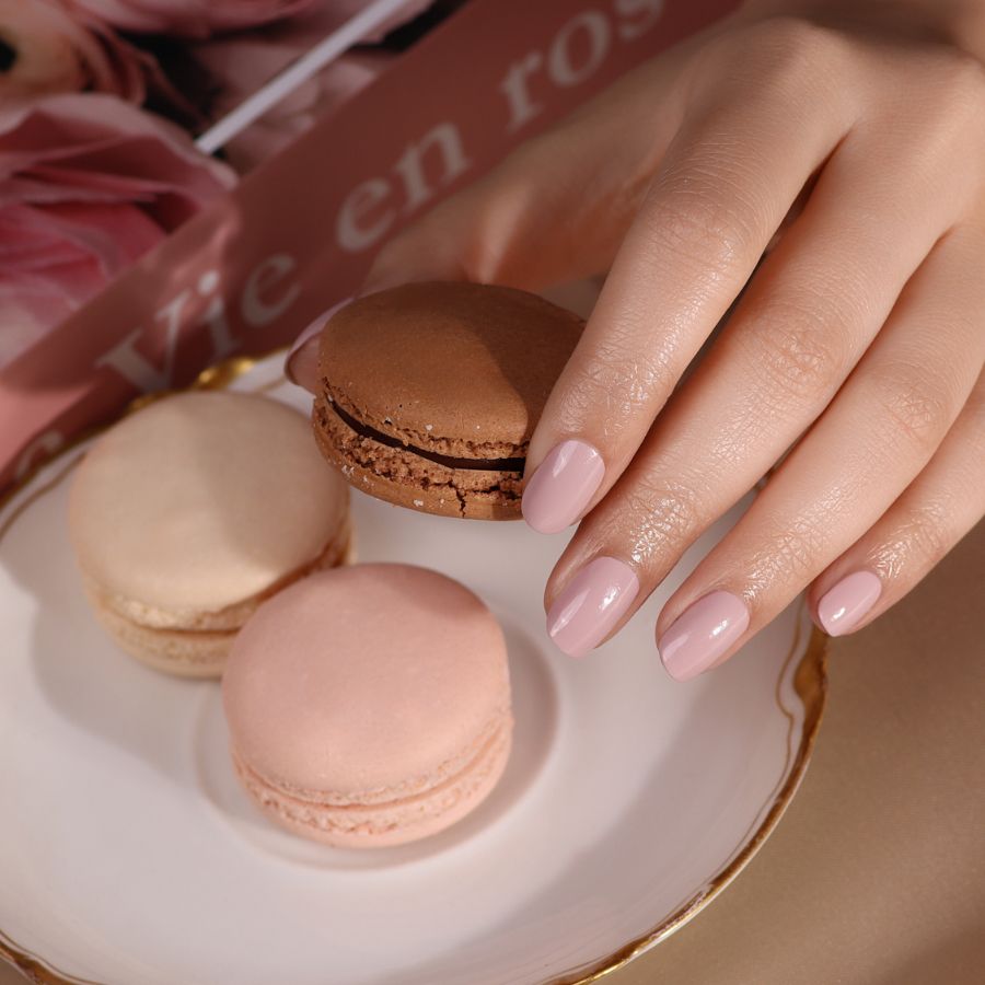 Hand mit lackierten Nägeln. Drei Makronen auf einem Teller.
