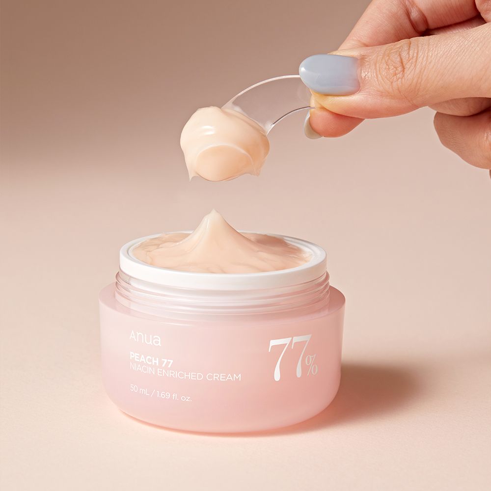 Eine Hand entnimmt ANUA Peach 77% Niacin Enriched Cream mit einem Spatel aus einem rosa Tiegel.