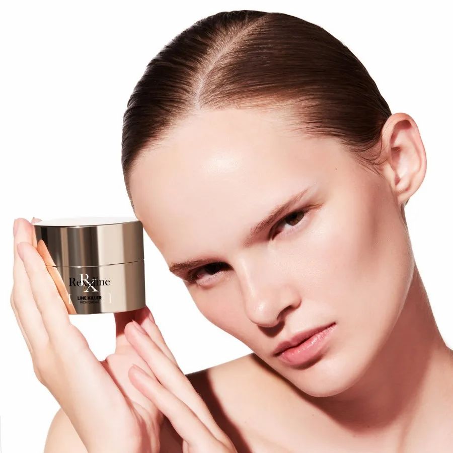 Frau hält Creme-Tiegel. Produkt: Rexaline Line Killer Rich Creme. Beige Dose mit goldfarbenem Deckel.