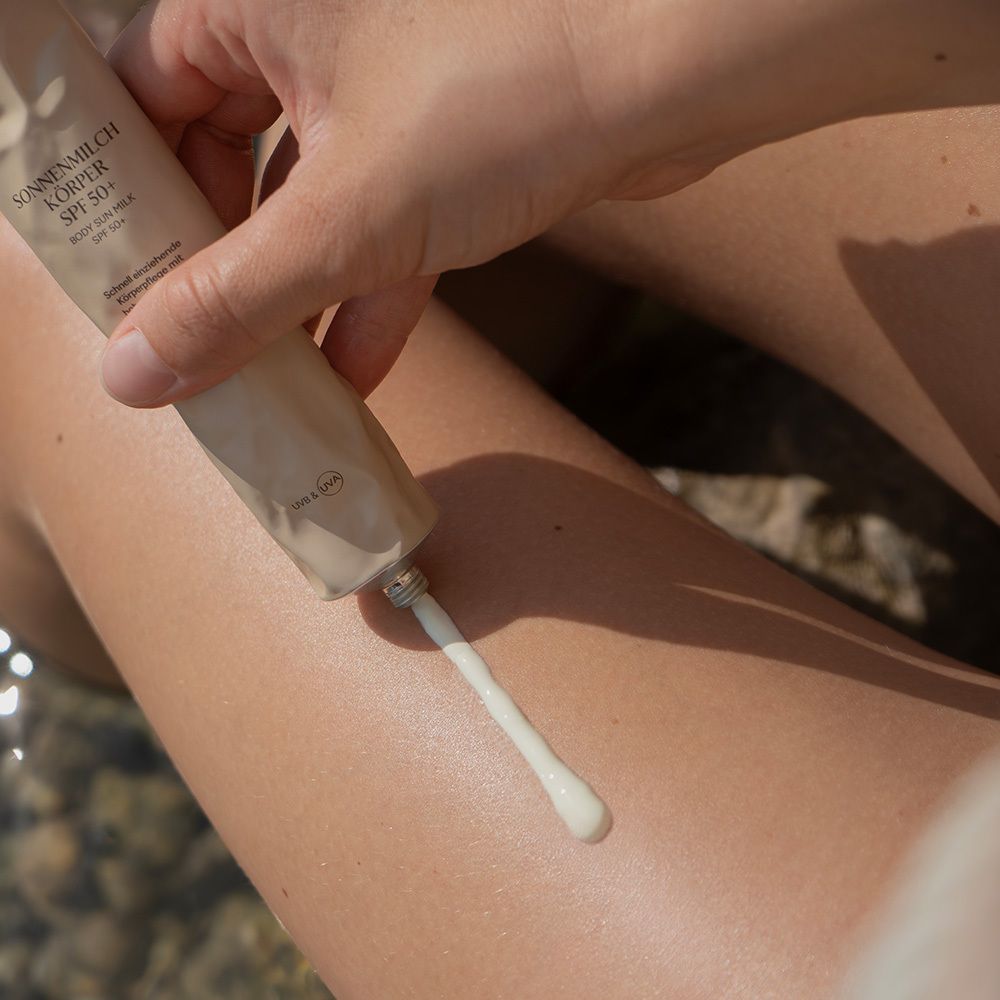 Person trägt Sonnenmilch auf Bein auf. Tube mit Aufschrift: SONNENMILCH KÖRPER SPF 50+. Creme wird aus Tube gedrückt.