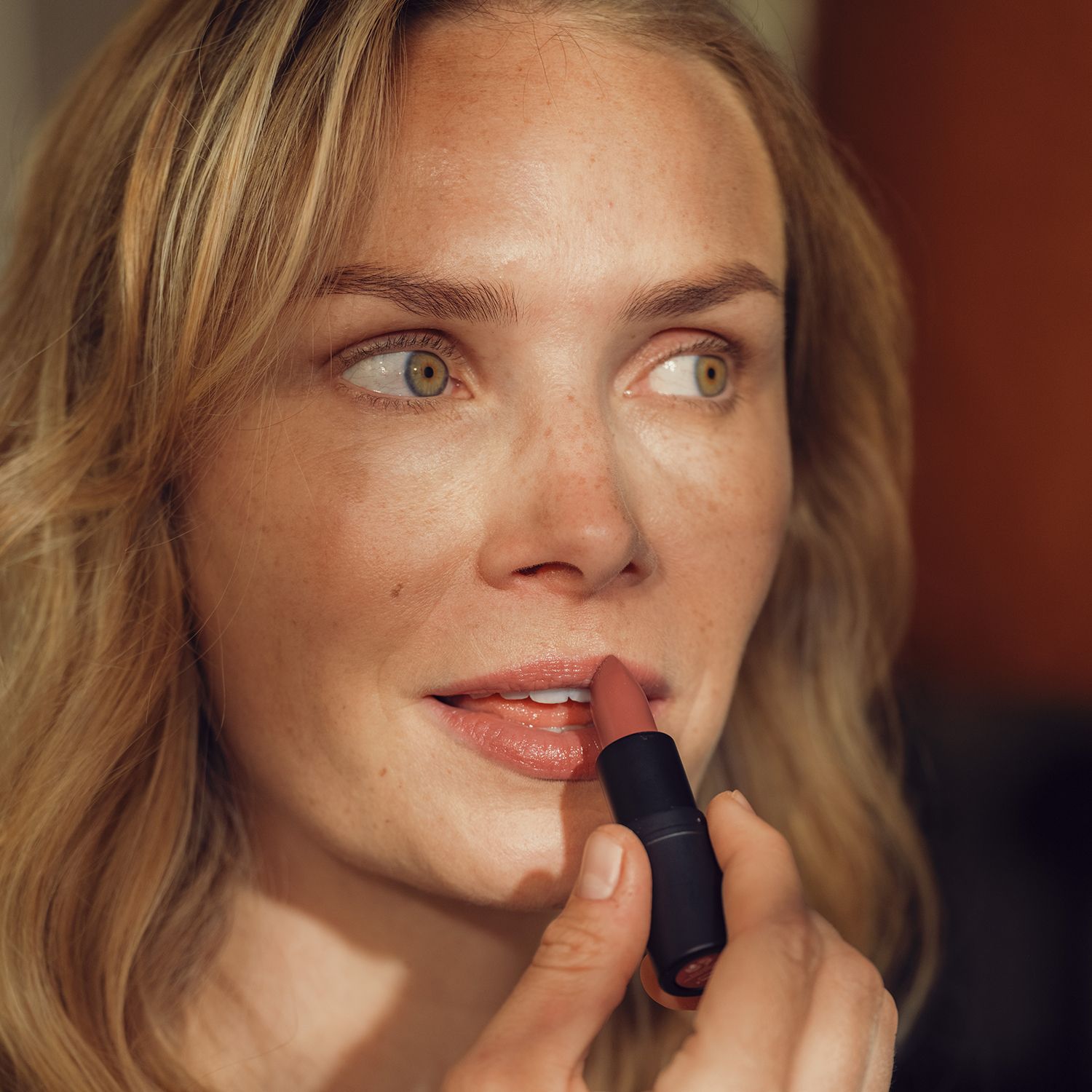 Frau trägt Hyaluron Lippenbalsam auf. Schwarzer Stift, farbiger Balsam. Gesicht nah.