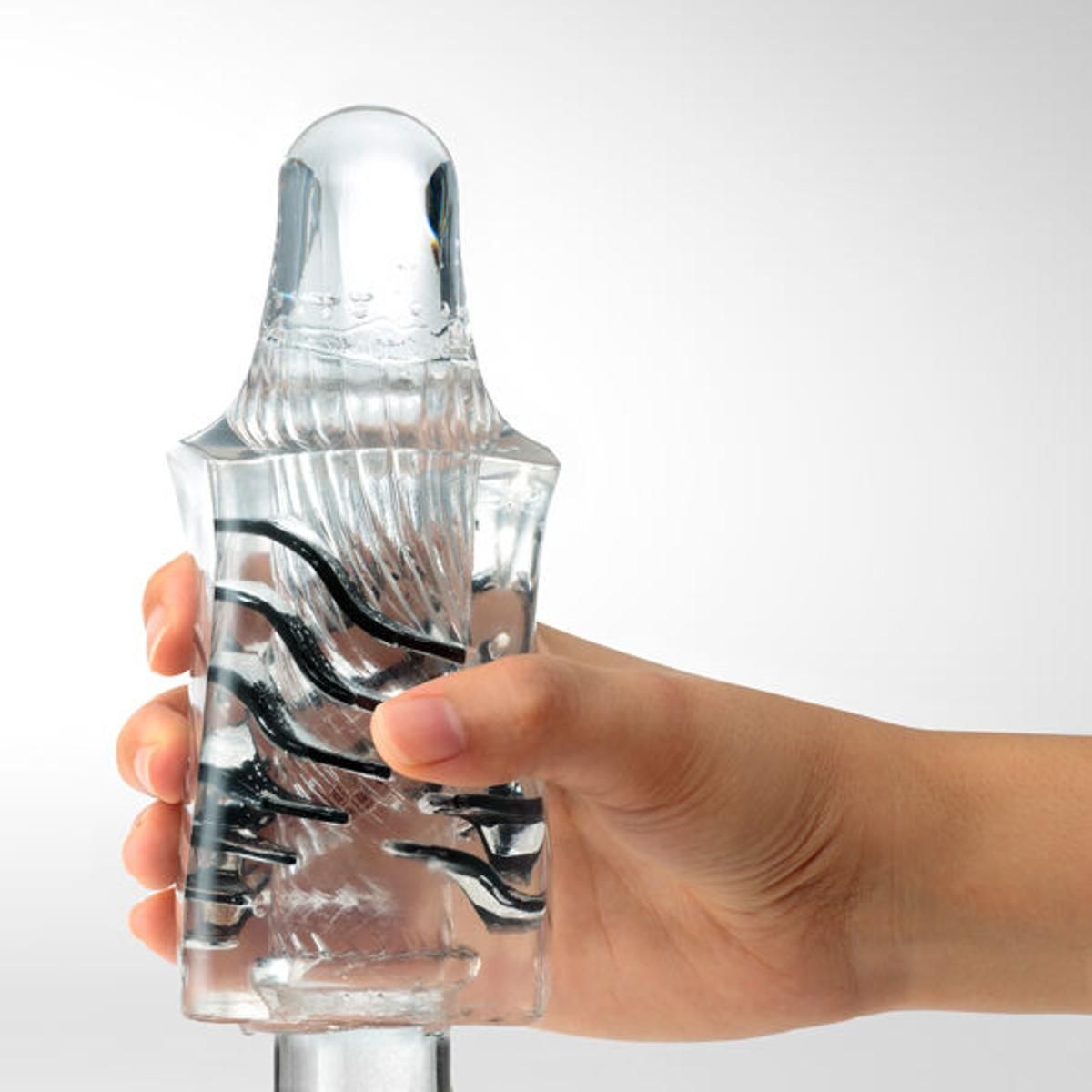 TENGA Crysta Leaf, transparentes Material, in Hand gehalten. Schwarze Elemente im Inneren. Oben abgerundet.