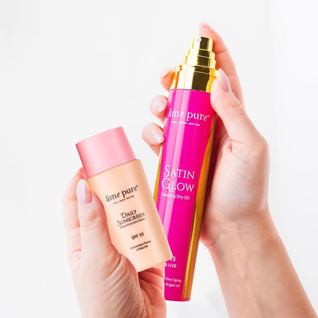 Hände halten Tages-Sonnenschutz SPF 50 und Satin Glow Bräunungsöl.