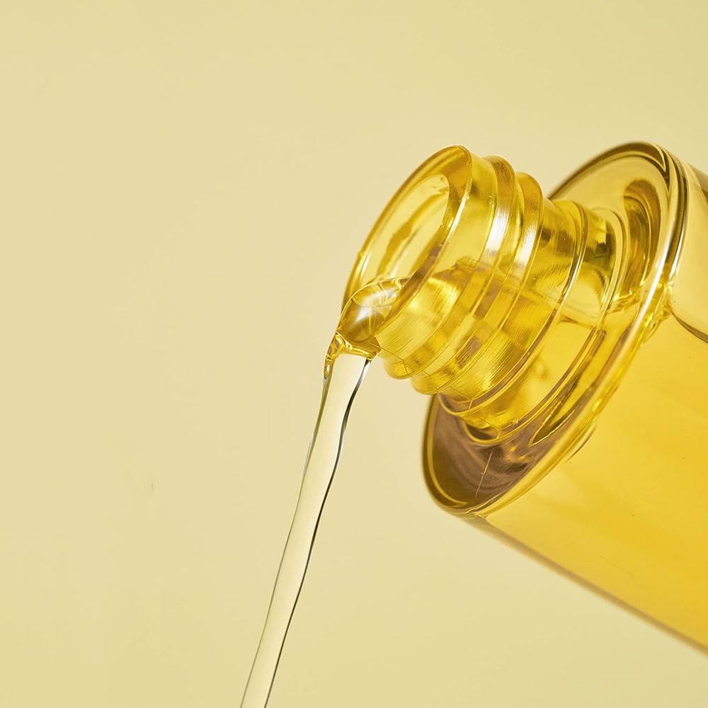 Gelbe Flüssigkeit fließt aus einer Flasche. Flaschenhals und Flüssigkeit sind im Fokus. Gelber Hintergrund.