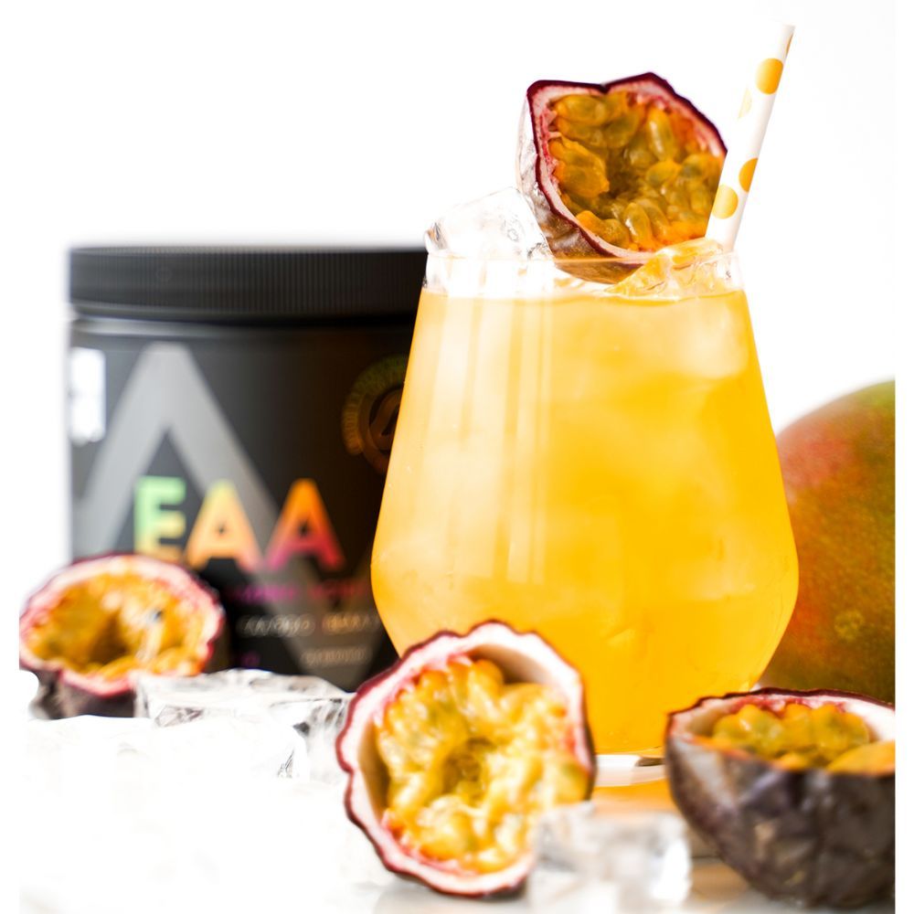 Glas mit gelbem Getränk, Eiswürfeln, Passionsfrucht und Strohhalm. Im Hintergrund Dose mit EAA-Aufschrift und Mango.