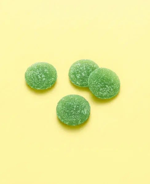 Vier grüne, runde Gummibärchen mit Zuckerbeschichtung auf gelbem Hintergrund.