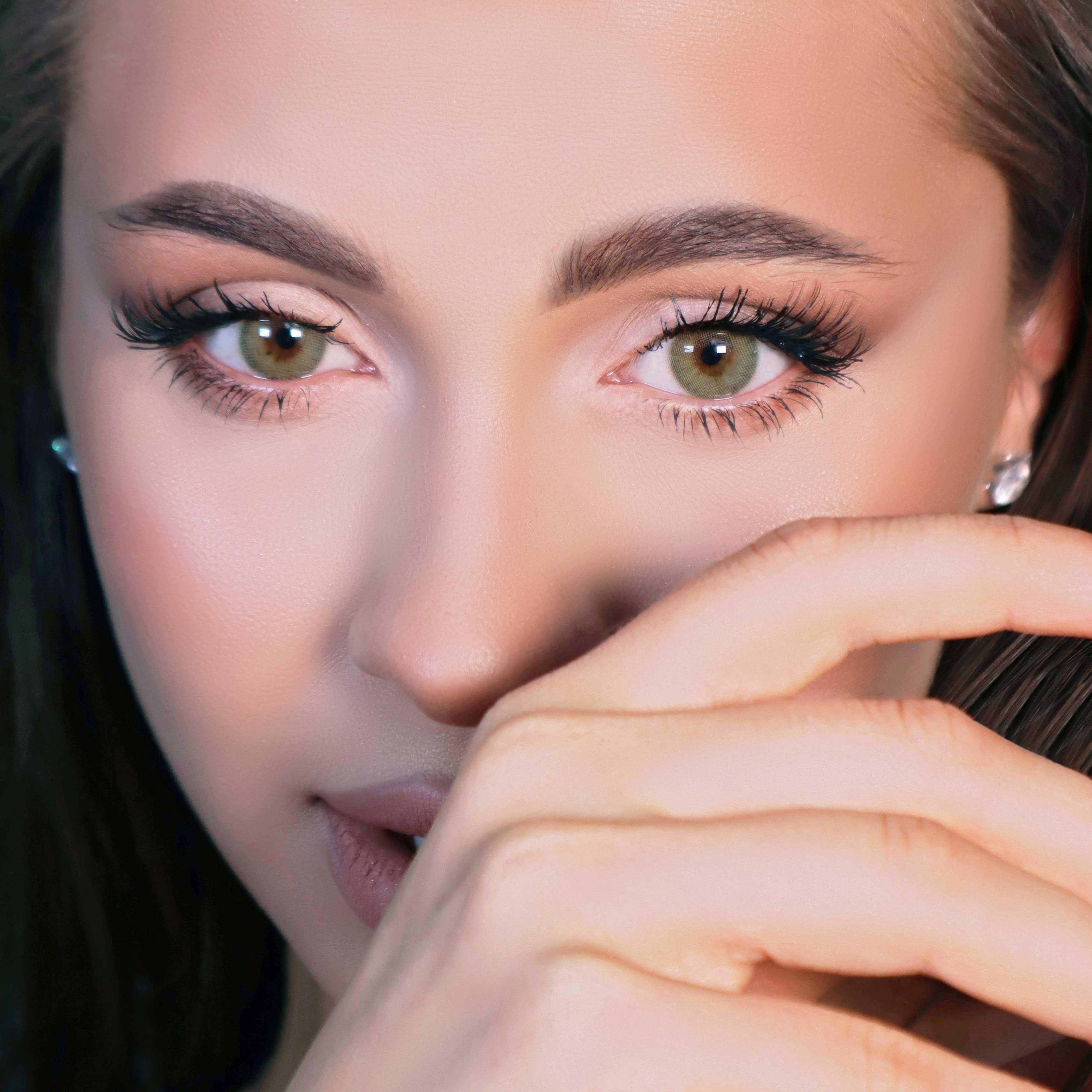 Nahaufnahme eines Gesichts mit grünen Kontaktlinsen. Die Frau hat Make-up. Hände sind im Bild. Fokus auf die Augen.