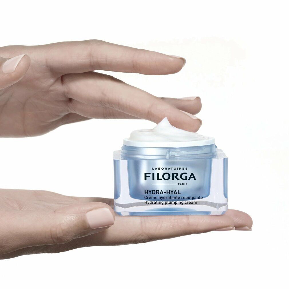 Hand hält Filorga Hydra-Hyal Creme-Gel. Transparenter Tiegel, blauer Inhalt, weißer Deckel.