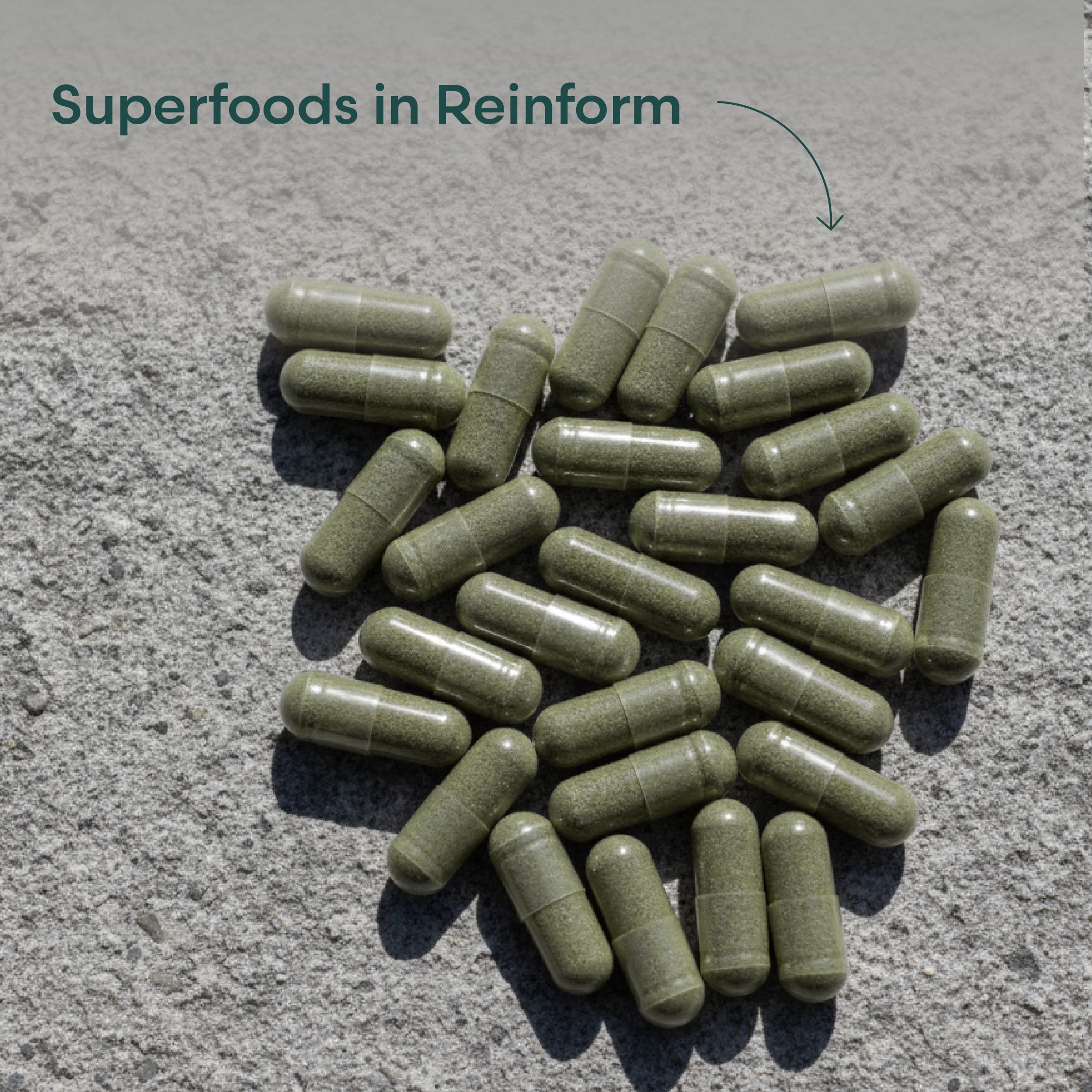 Haufen grüner Kapseln auf grauem Untergrund. Kapseln enthalten Pulver. Beschriftung: Superfoods in Reinform.