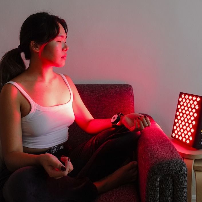 Frau sitzt mit Lichttherapiegerät. Sie trägt ein Armband. Gerät strahlt rotes Licht.