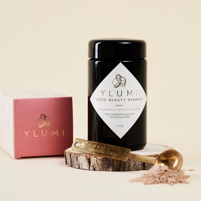 Schwarzes Glas, rosa Schachtel, goldener Messlöffel. Aufschrift: YLUMI COCO BEAUTY SPARKLE. Nahrungsergänzungsmittel.