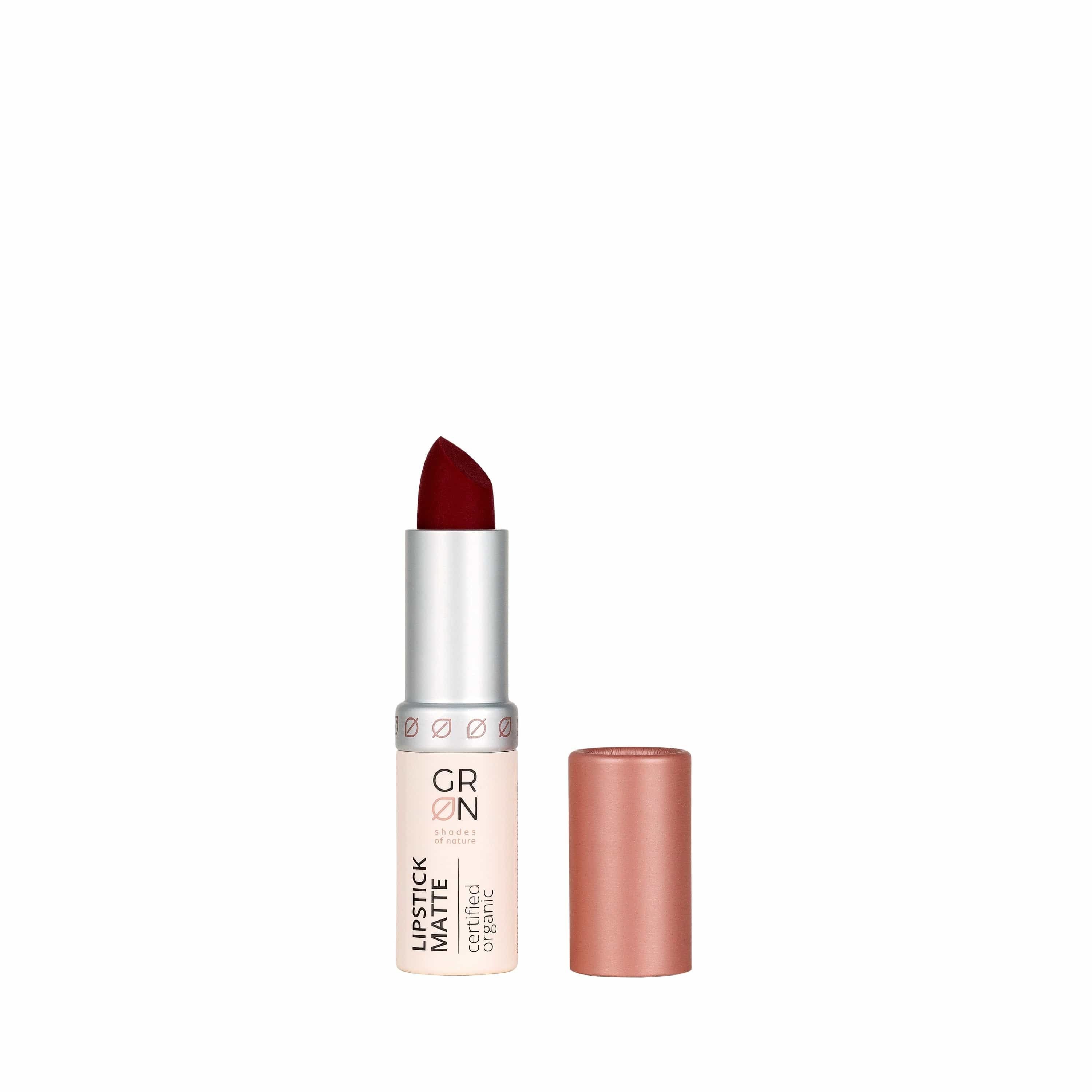 Lippenstift, geöffnet, mit dunkelroter Spitze. Silberne Hülse mit Schriftzug GRN und Zertifizierung. Rosafarbene Kappe daneben.