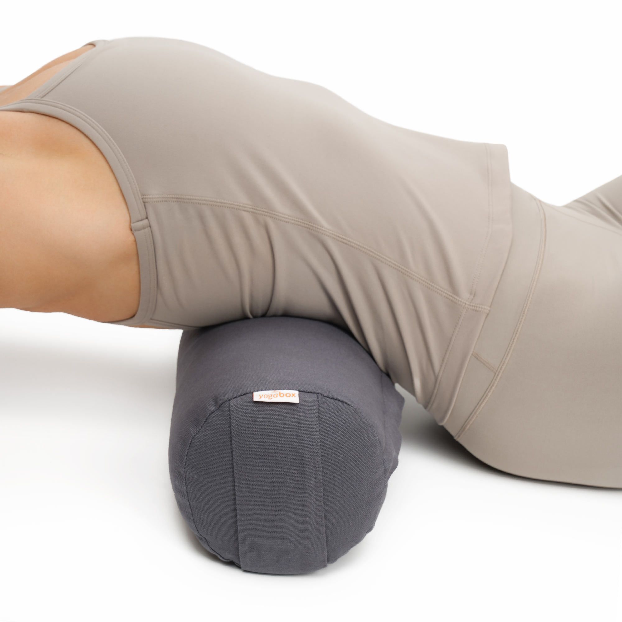 Grauer Yogabolster unter dem Rücken einer liegenden Person, zur Unterstützung.