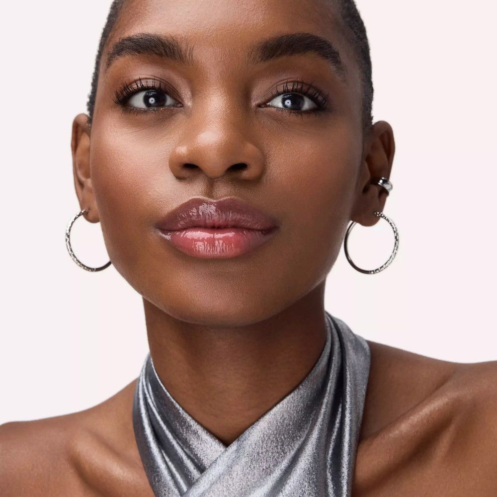 Porträt einer Frau mit glänzenden Lippen. Silberner Ohrring. Keine Marke oder Produktname sichtbar.