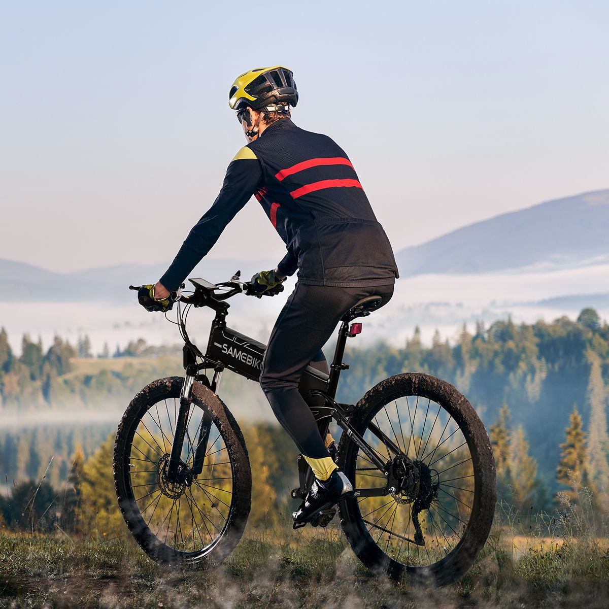 Person fährt auf einem schwarzen E-Bike. Trägt Helm und Sportkleidung. Landschaft im Hintergrund.