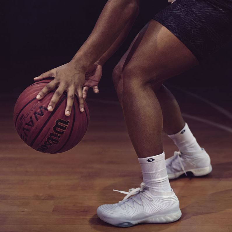 Person spielt Basketball. Weiße Kompressionssocken und Sportschuhe. Ball wird gedribbelt.