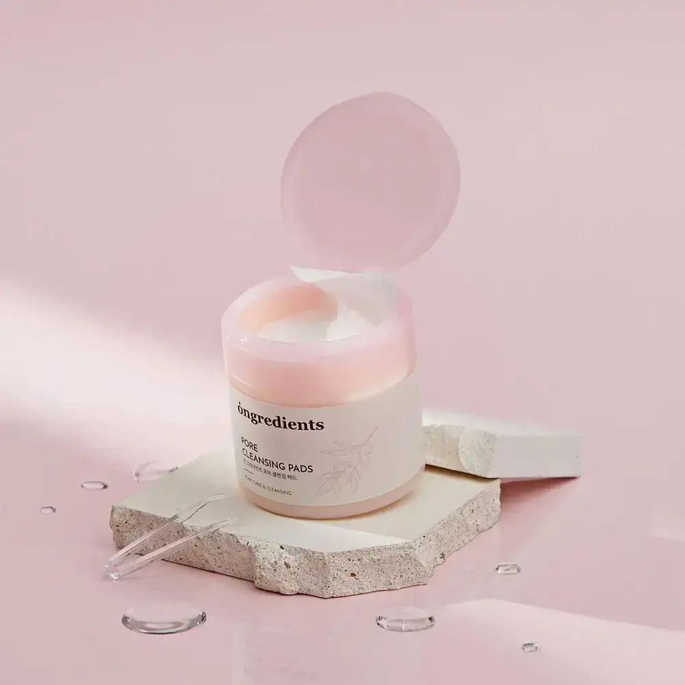 Behälter mit rosa Deckel, geöffnet. Aufschrift "ongredients Pore Cleansing Pads". Auf Stein platziert. Rosa Hintergrund.
