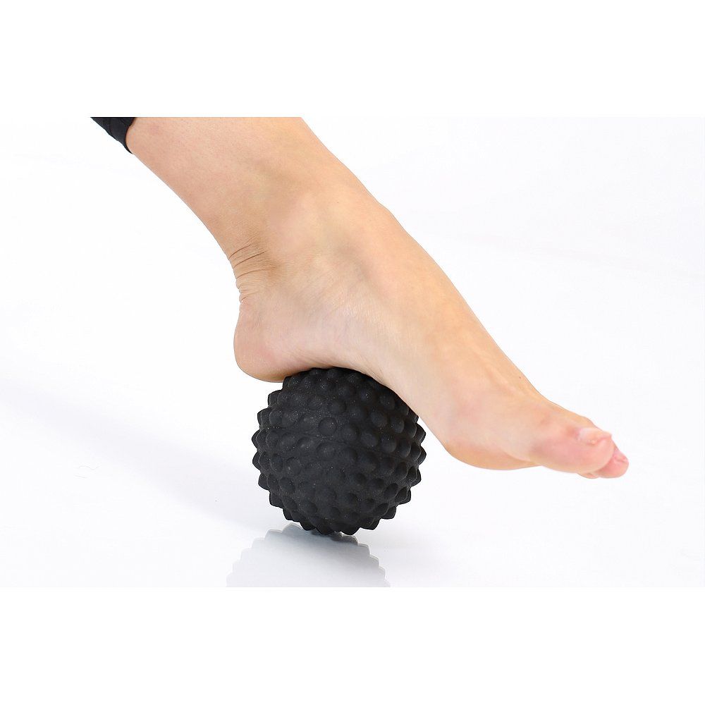 Schwarzer Faszienball mit Noppen unter dem Fuß.