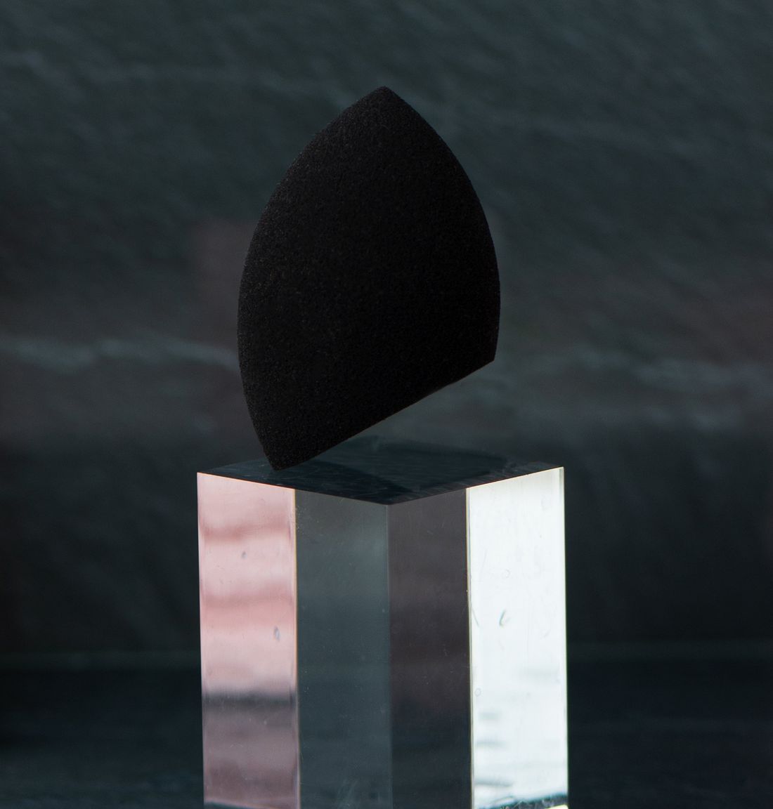 Schwarzer Beauty Blender auf einem transparenten Podest.